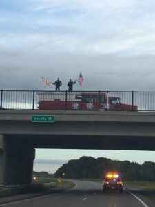 Firefighters and a fire truck on an overpass honoring the funeral escort.